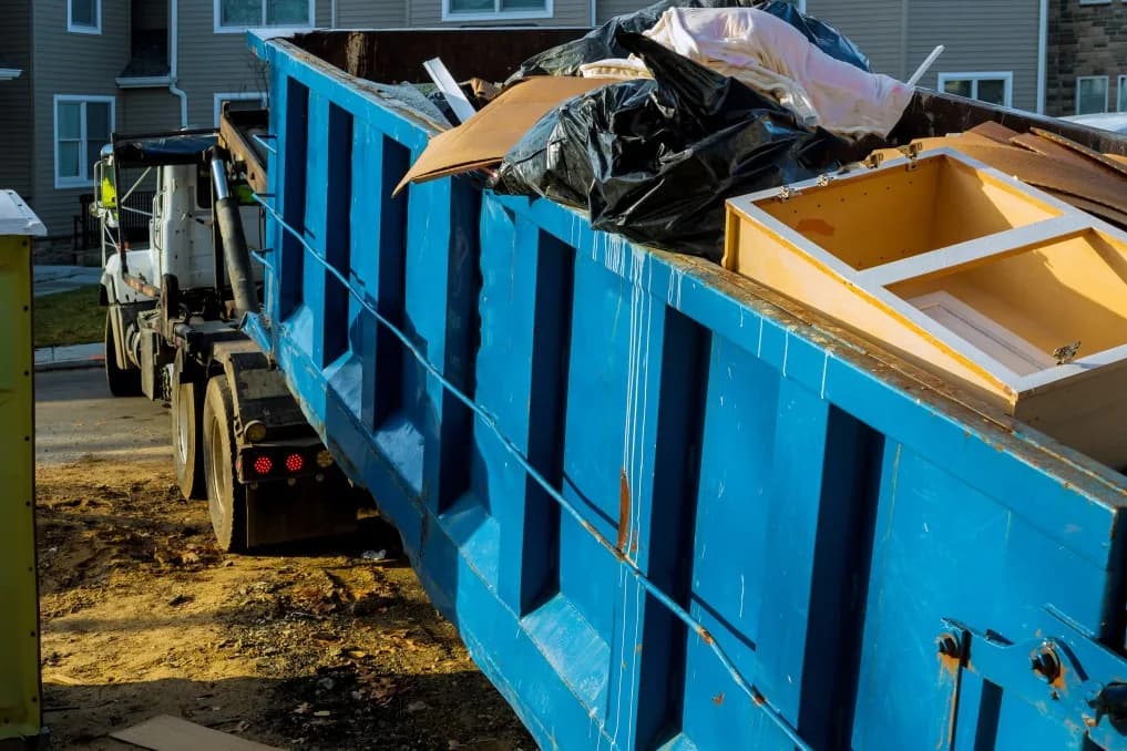 Old furniture, mattresses, and cleanout debris piled beside a roll-off dumpster