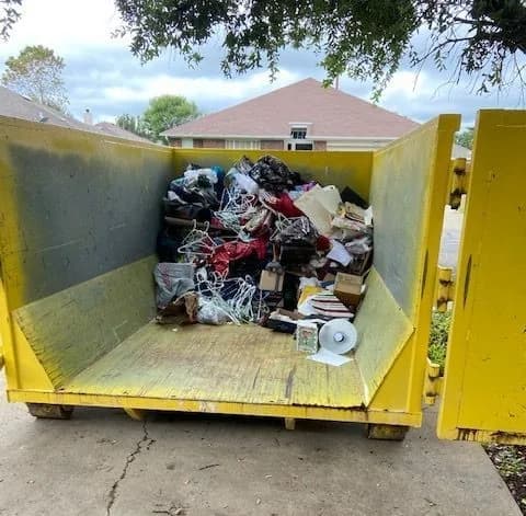 Excavator loading heavy debris into a roll-off dumpster on a demolition site
