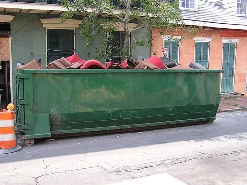 Green roll-off dumpster on a paved driveway ready for a weekend home project