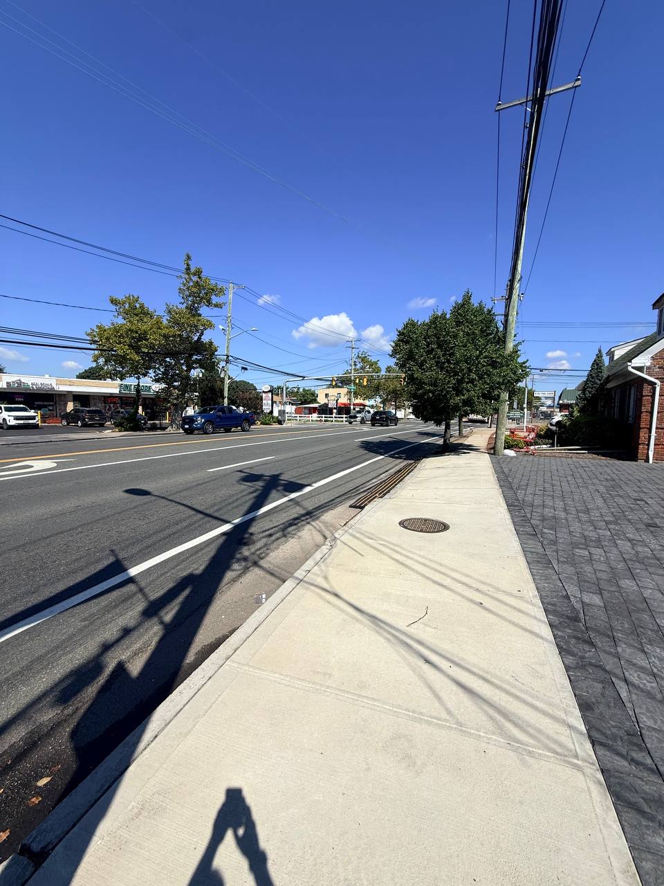 A wide repaved South Shore commercial road on Long Island near Oceanside and Long Beach Road, with storefronts, a fresh sidewalk, utility poles and a clear blue sky.