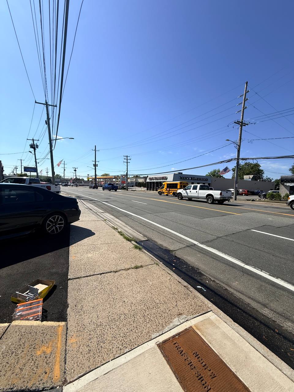A busy South Shore Long Island commercial strip near Long Beach Road with storefronts, a gas station, a school bus and traffic under a bright sky.